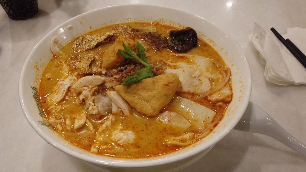 Steaming bowl of Chicken Laksa Noodle Soup with rich coconut curry broth, chicken, noodles, and herbs at PappaRich restaurant in Parramatta, Sydney