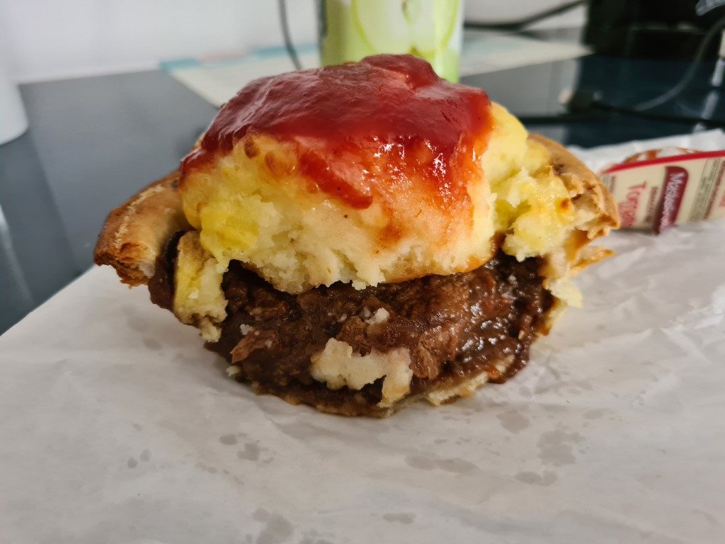 Close-up of Quinney's Gourmet Pies famous Meat and Potato Pie cut open, revealing chunky beef filling in rich gravy with creamy mashed potato topping drizzled in tomato sauce, Surfers Paradise, Gold Coast