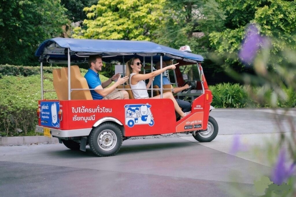 MuvMi electric tuk-tuk in Bangkok with Western tourists riding through green park area