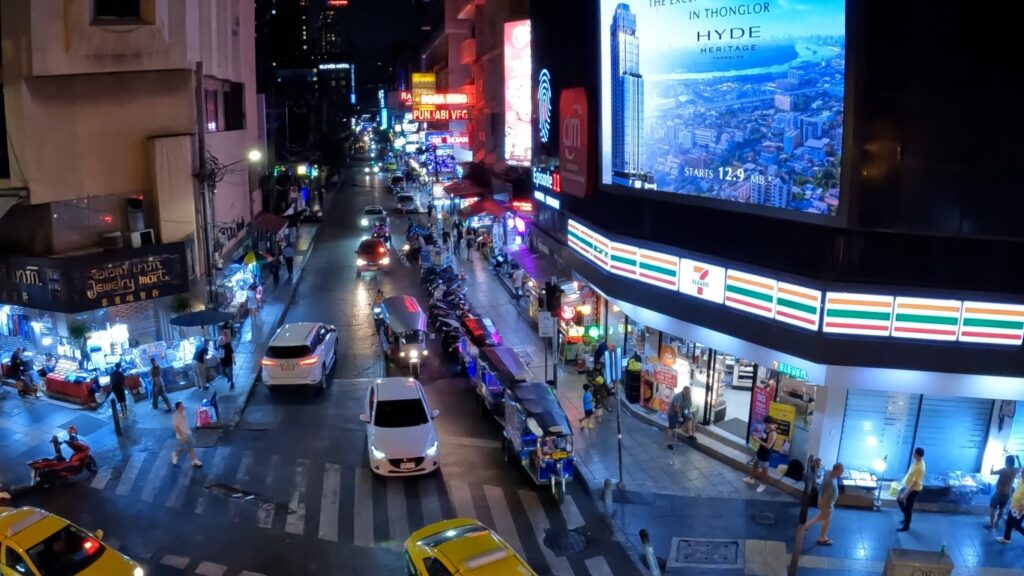 Nighttime view looking down Soi 11 Sukhumvit Bangkok nightlife area from Nana BTS skybridge with neon lights, bars, and crowds