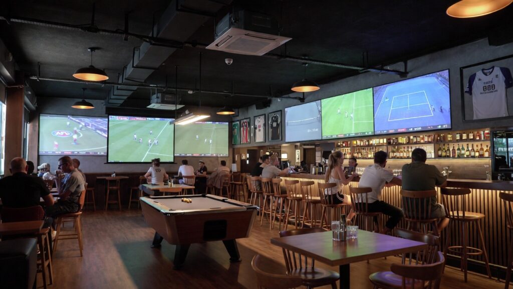 Lively sports bar in Phuket filled with excited crowds watching the Australian Open tennis on multiple large screens, with cold beers and a vibrant atmosphere perfect for live sports viewing